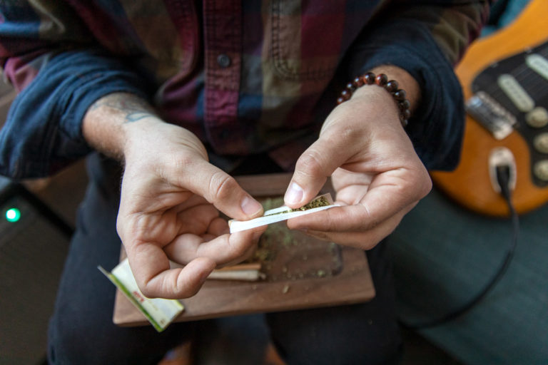 A Man Rolling A Joint with a Guitar in the background out of focus