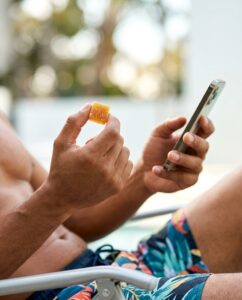 Man relaxing poolside holding an Insa cannabis gummy and his phone — fast-acting cannabis edibles Connecticut