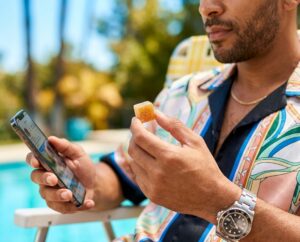 Man poolside in a tropical shirt holding an Insa cannabis chew gummy — premium cannabis edibles now available at Connecticut dispensaries