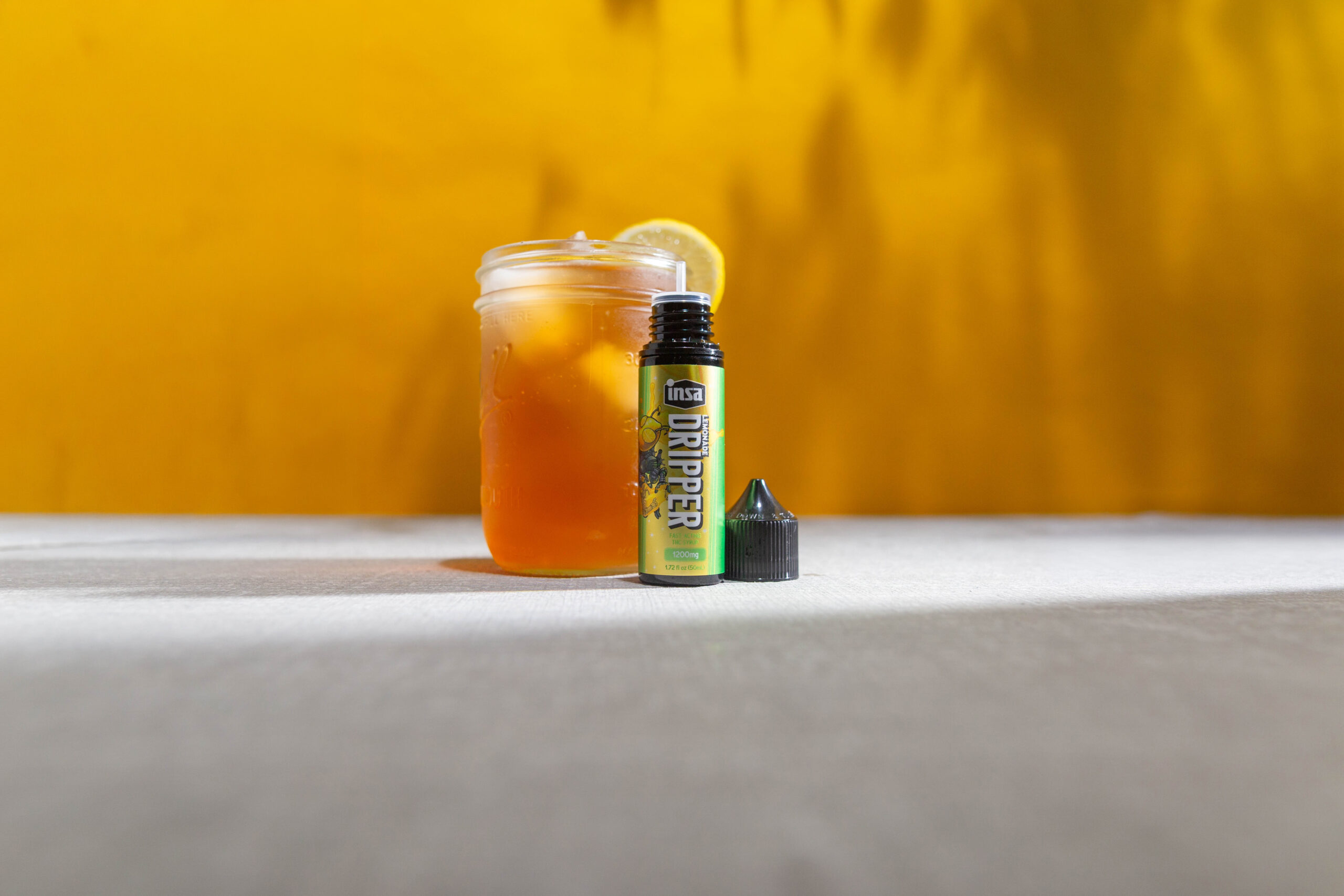 A Caddy Cooler beverage in a glass next to a bottle of Insa Lemonade Dripper