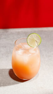 A Peach Grapefruit Fizz drink in a glass filled with ice and a lime wedge.